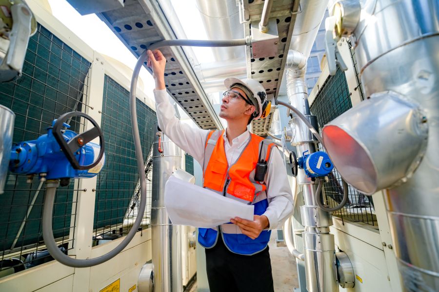 Ingénieur inspectant un plafond d'usine industrielle avec système de ventilation et éclairage.